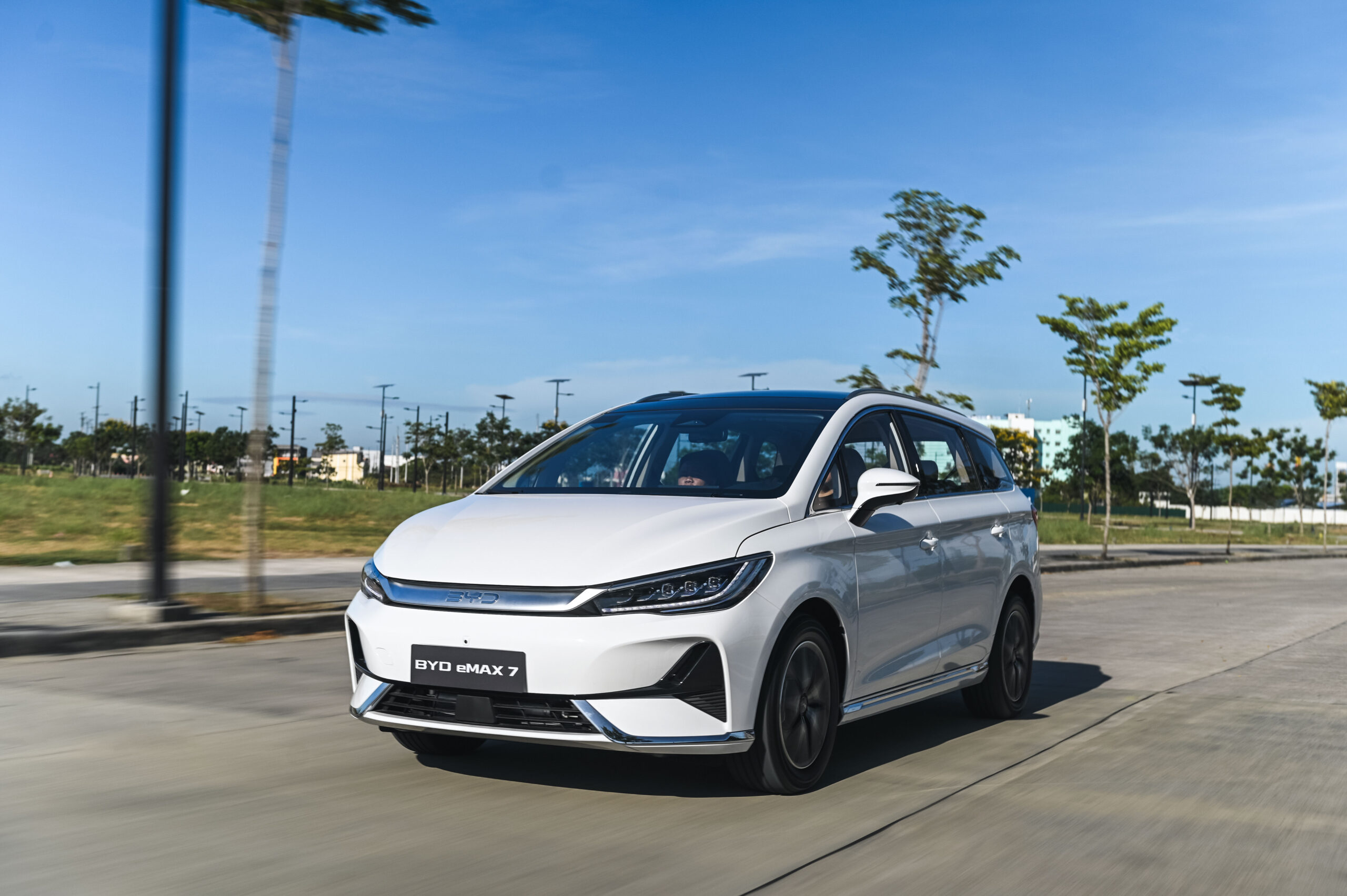 This is the BYD e-MAX 7, an electric MPV with a front wheel drive Powertrains. This car in the photo is on a clean rod with some small trees in the background under a bright daylight.